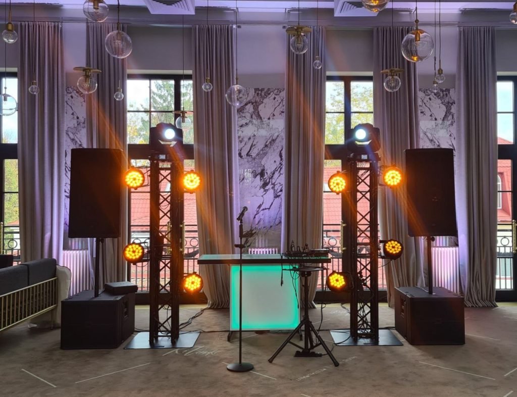 Professional DJ setup with subwoofers, truss towers, LED lighting, and central booth